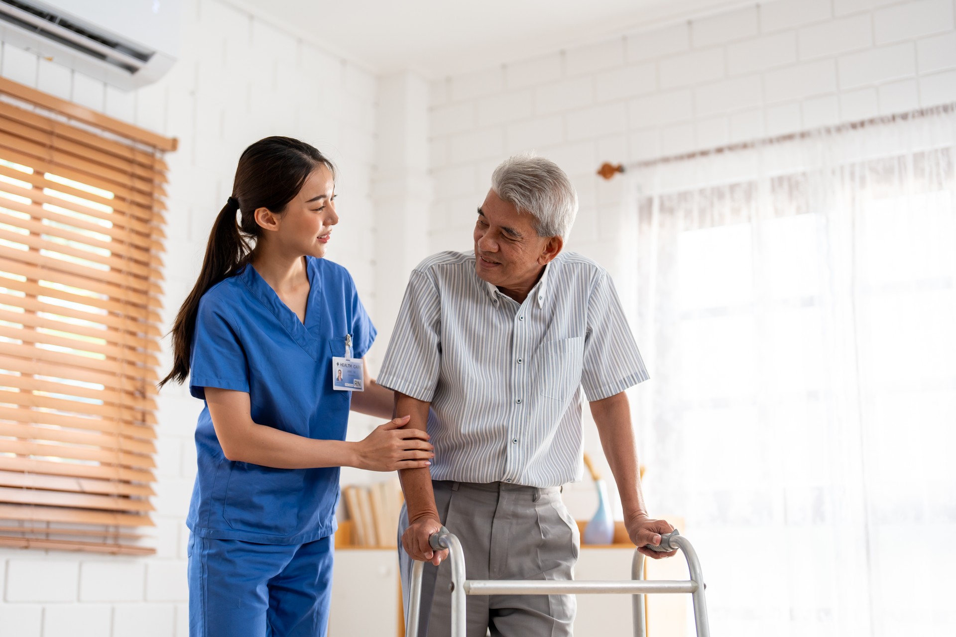 Asian senior elderly man patient doing physical therapy with caregiver. Attractive specialist carer women help and support older mature male practice walking slowly with walker at nursing home care.